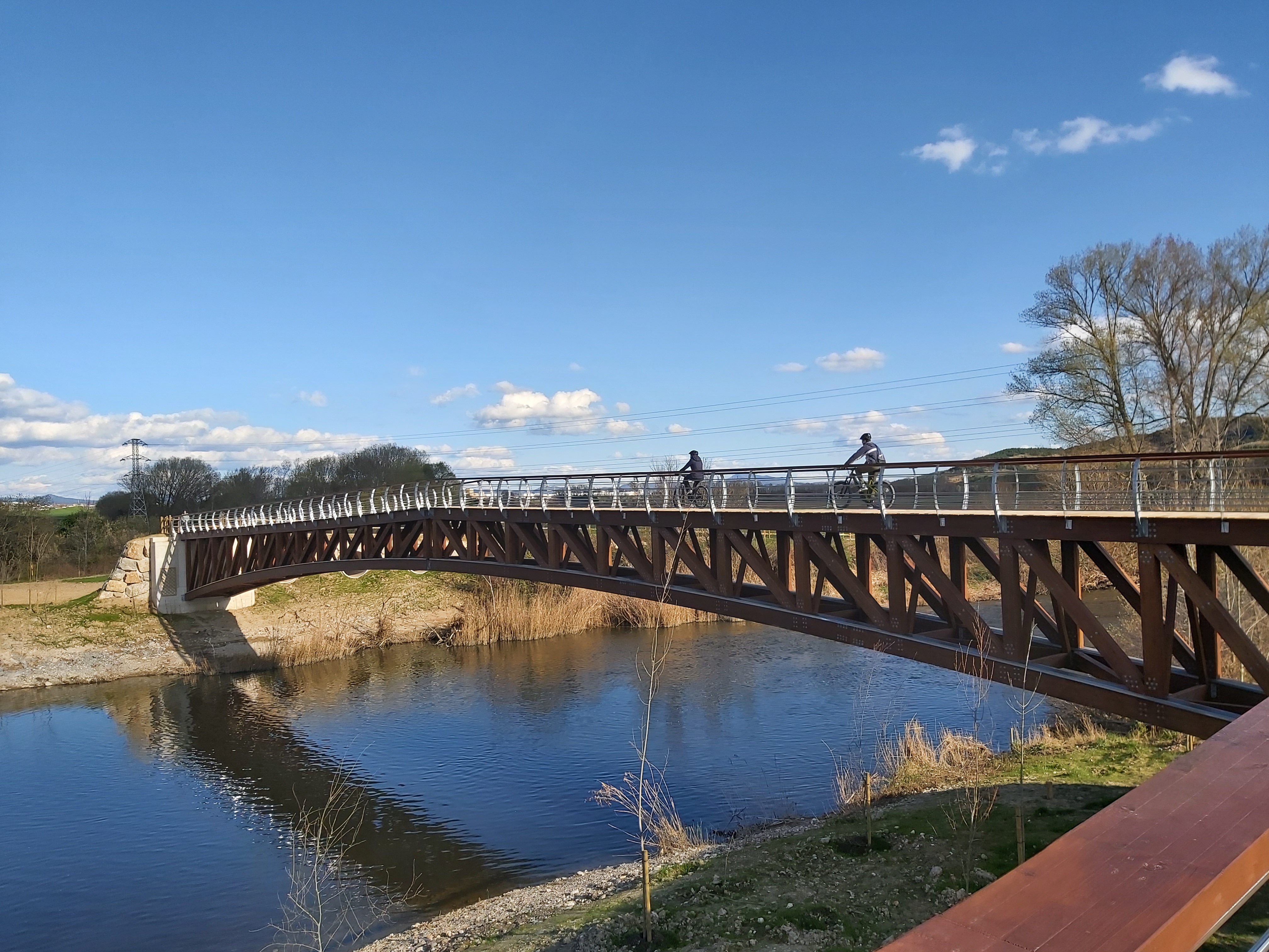 Dos ciclistas cruzando un puente sobre el río Arga